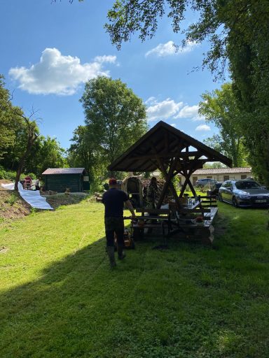 Ein Mann steht vor einem Unterstand in einer grünen Umgebung, umgeben von Bäumen.