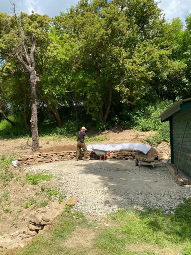 Ein Mann arbeitet an einem Gartengrundstück mit Bäumen im Hintergrund.