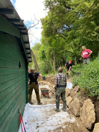 Männer arbeiten an einem Gartenprojekt in einem bewaldeten Gebiet.
