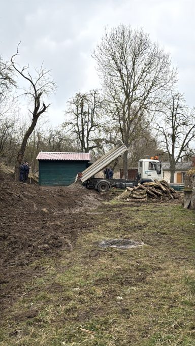 Bauarbeiten auf einem Grundstück mit einem grünen Schuppen und Baumaschinen im Hintergrund.