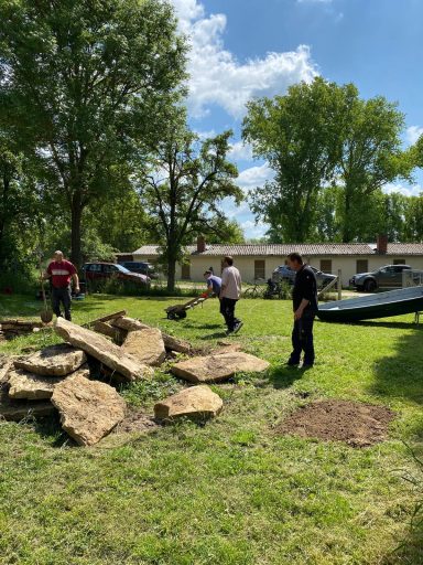 Personen arbeiten im Freien, heben große Steine und räumen das Grundstück auf.