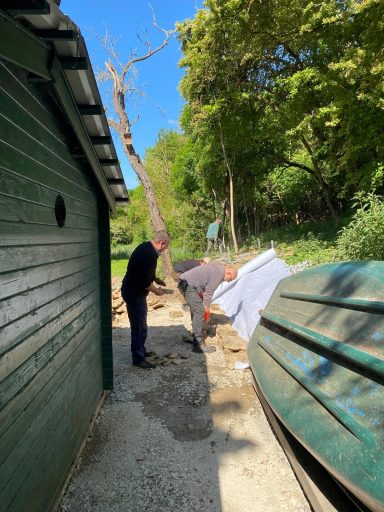 Zwei Personen arbeiten an einem Bauprojekt neben einer grünen Wand und einem Baum.