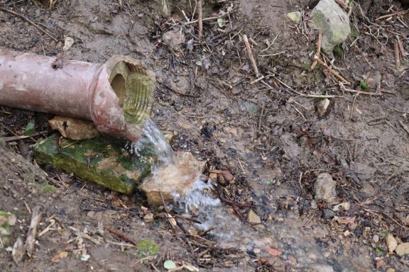 Ein Rohr leitet Wasser auf einen erdigen Boden mit Moos und kleinen Steinen.