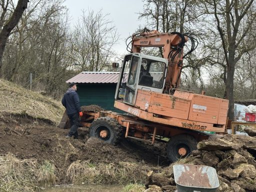 Ein Arbeiter steuert eine orangefarbene Baumaschine auf unebenem Terrain.