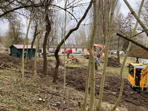 Landschaft mit Bäumen, einem Baugerät und Menschen bei Gartenarbeiten.