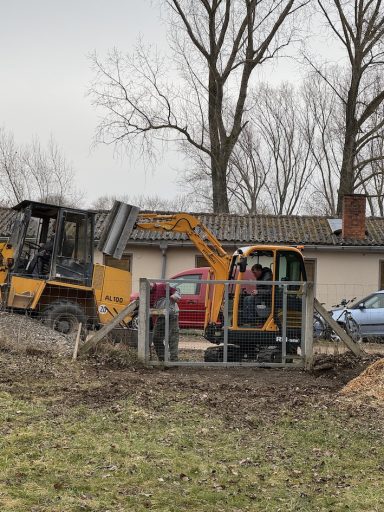 Bagger und Muldenkipper arbeiten auf einer Baustelle mit Bäumen im Hintergrund.