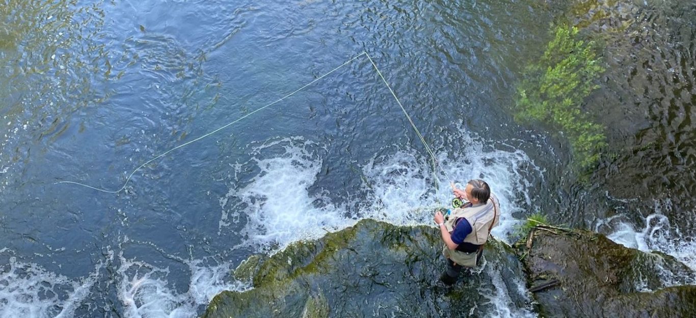 Angler/Fliegenfischer an einem felsigen Ufer mit fließendem Wasser.